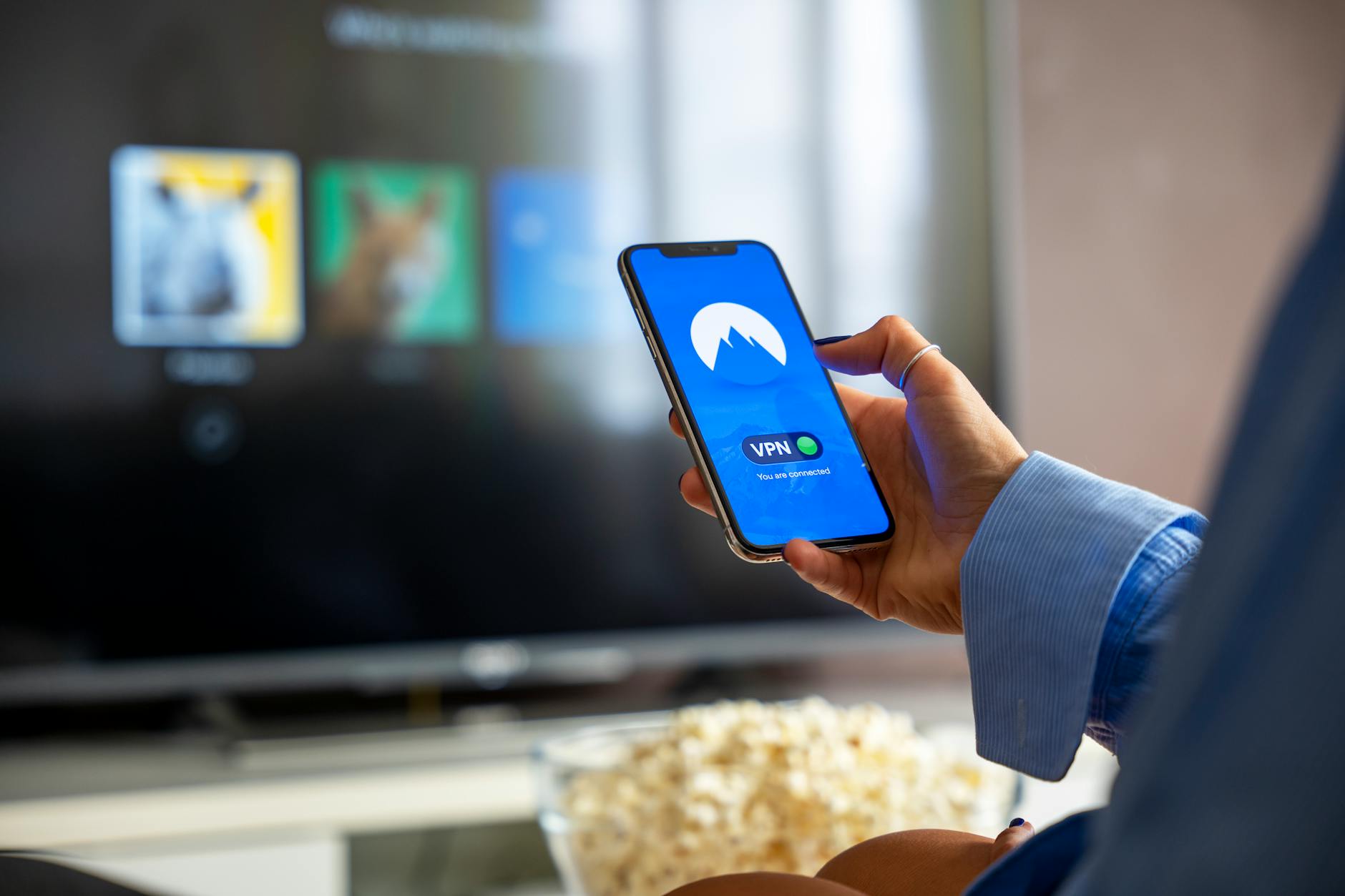 Hand holding streaming device remote control with Netflix interface on television screen