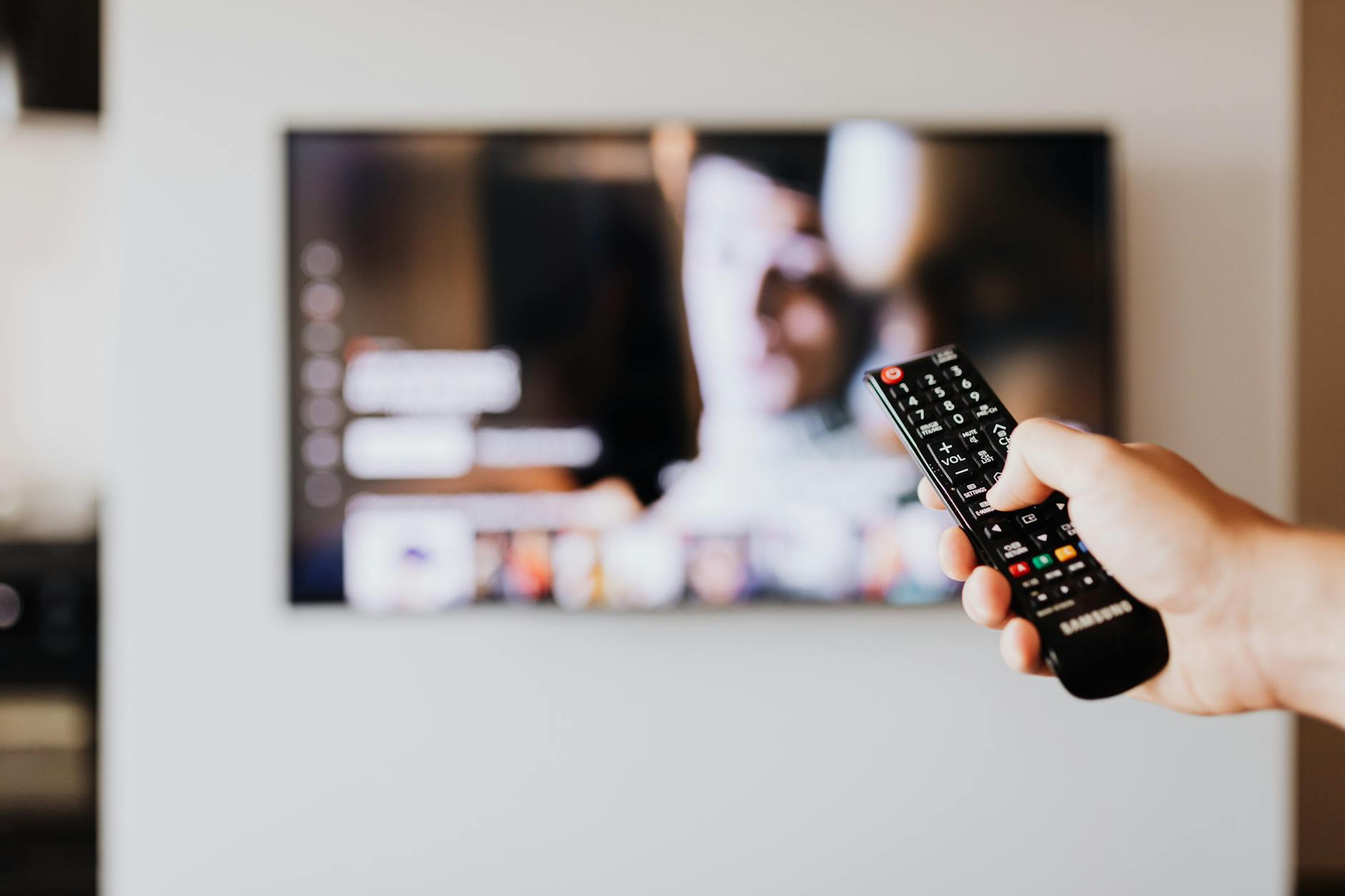 Hand holding television remote control pointed at large screen display