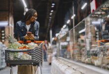 Person pushing a grocery cart through a supermarket aisle