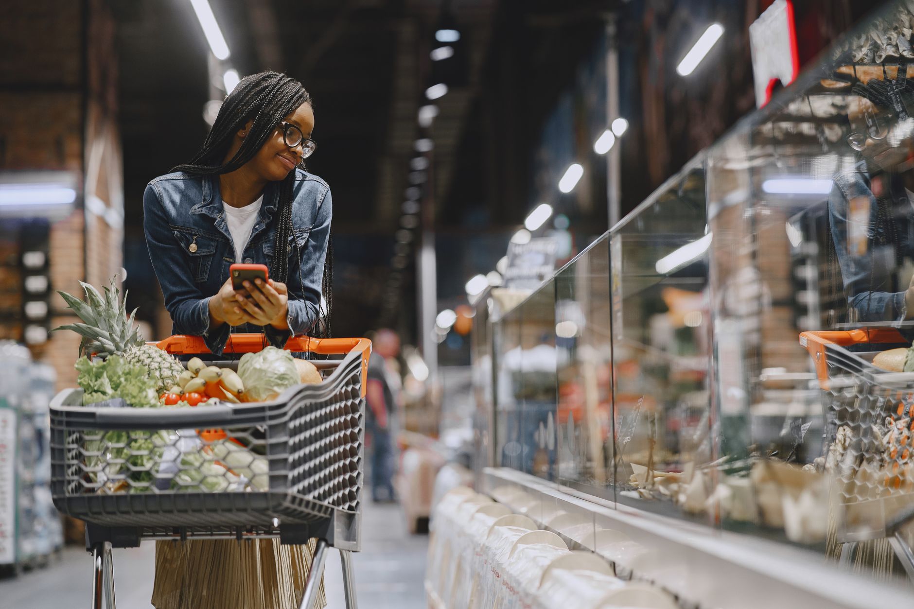 Person pushing a grocery cart through a supermarket aisle